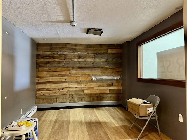 empty room with wood walls, a textured ceiling, baseboards, and wood finished floors