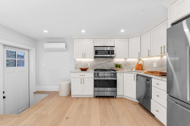 kitchen with white cabinets, stainless steel appliances, light hardwood / wood-style floors, sink, and a wall mounted AC