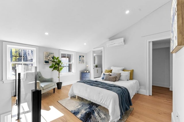 bedroom featuring lofted ceiling, light wood-type flooring, and a wall mounted air conditioner