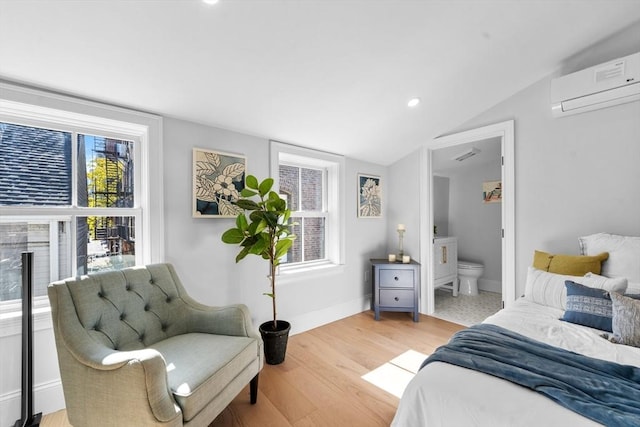 bedroom featuring ensuite bathroom, a wall mounted AC, light wood-type flooring, and multiple windows