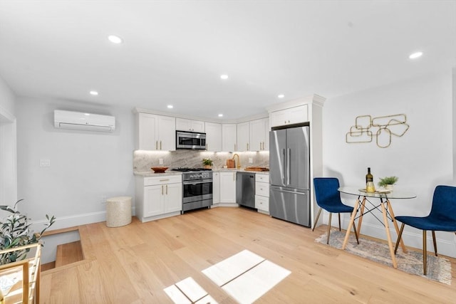 kitchen with tasteful backsplash, light hardwood / wood-style flooring, a wall mounted air conditioner, stainless steel appliances, and white cabinets