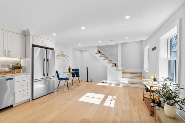 kitchen with tasteful backsplash, appliances with stainless steel finishes, white cabinetry, and light hardwood / wood-style floors