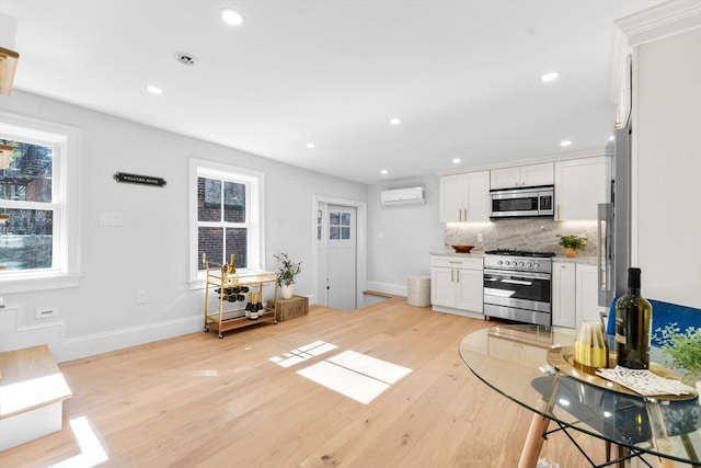 kitchen with an AC wall unit, white cabinetry, stainless steel appliances, light hardwood / wood-style floors, and backsplash