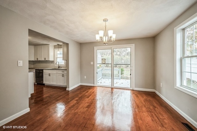 unfurnished dining area with a textured ceiling, plenty of natural light, dark wood-type flooring, and an inviting chandelier