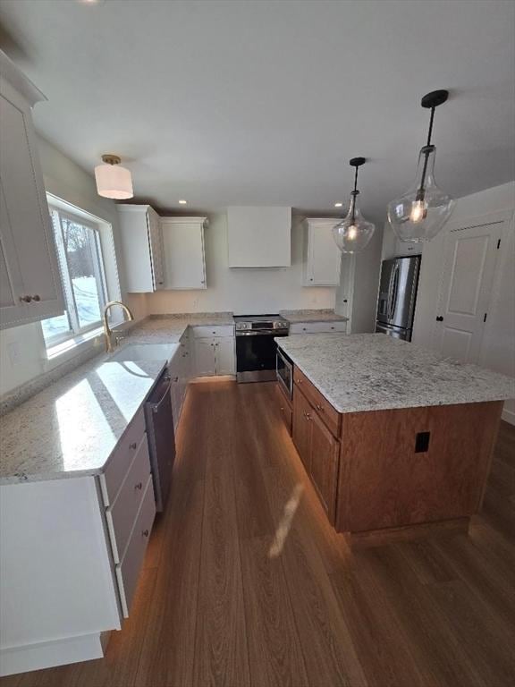 kitchen with stainless steel appliances, white cabinetry, a kitchen island, and hanging light fixtures