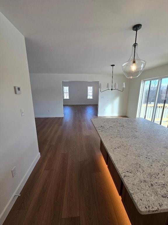 interior space featuring a center island, dark hardwood / wood-style floors, pendant lighting, and light stone counters