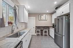 kitchen with sink, light tile patterned floors, white cabinetry, stainless steel appliances, and light stone counters