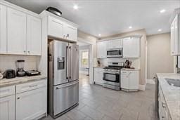 kitchen featuring light tile patterned floors, stainless steel appliances, light stone countertops, white cabinets, and decorative backsplash