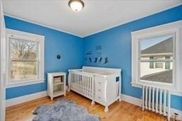 bedroom featuring multiple windows, crown molding, radiator, and hardwood / wood-style floors