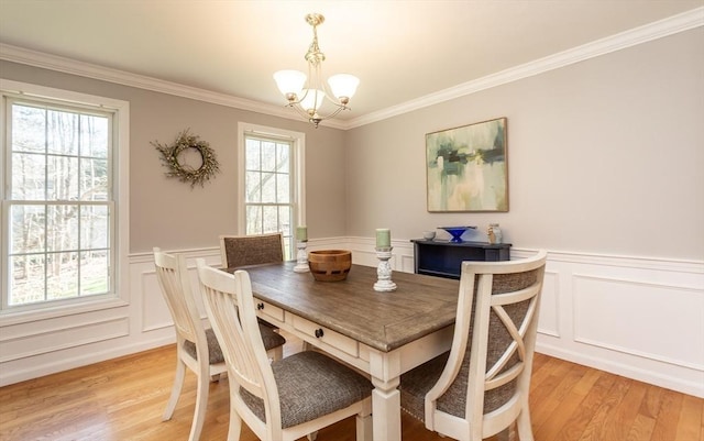 dining room featuring light wood-style flooring, wainscoting, a notable chandelier, crown molding, and a decorative wall