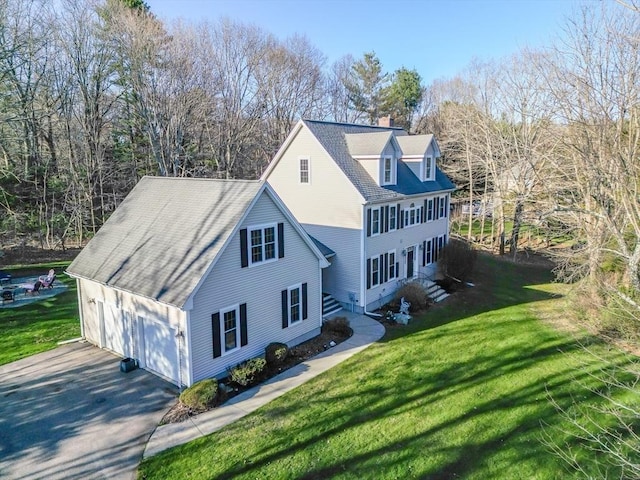 view of side of home with a yard, driveway, a shingled roof, and a chimney
