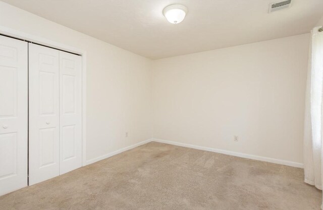 unfurnished bedroom featuring light carpet, baseboards, visible vents, and a closet