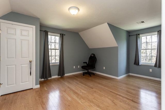 additional living space with baseboards, vaulted ceiling, visible vents, and light wood-style flooring