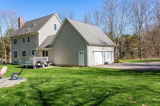 exterior space with a chimney, a wooden deck, a lawn, roof with shingles, and a garage