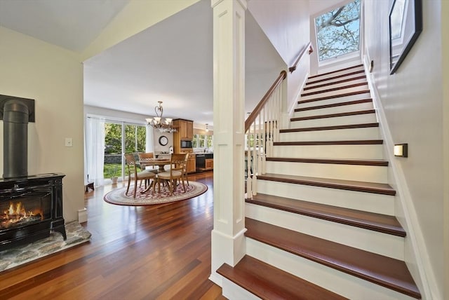 staircase with wood finished floors, a chandelier, and a wood stove