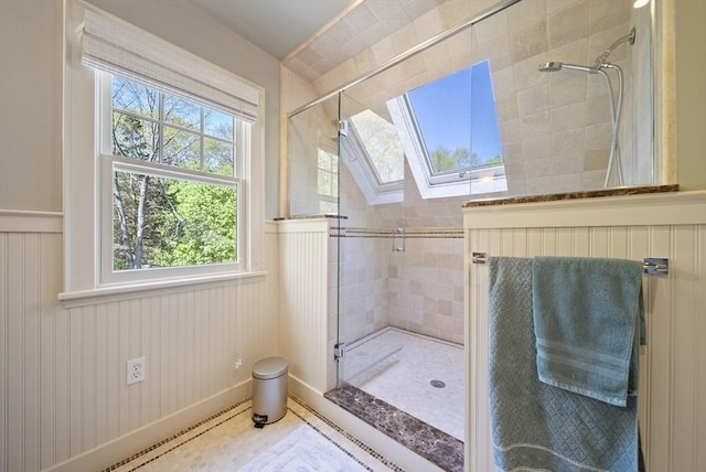 full bath featuring a shower stall, a skylight, and a wainscoted wall