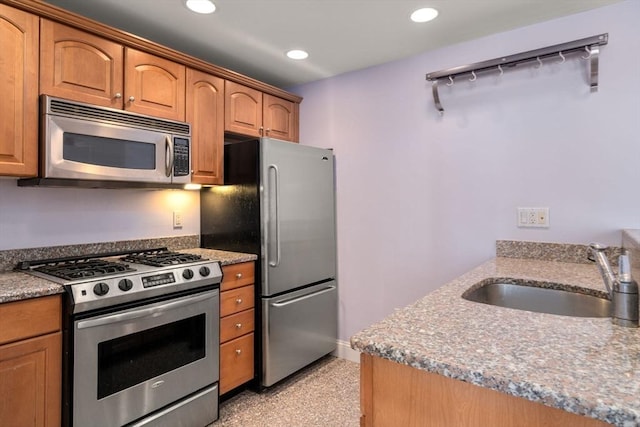 kitchen with light stone countertops, recessed lighting, appliances with stainless steel finishes, brown cabinets, and a sink