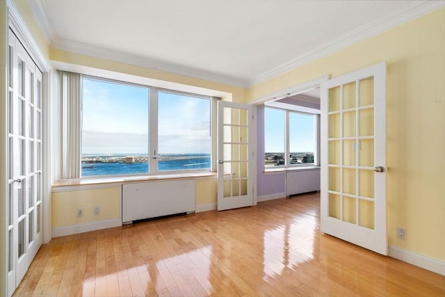 spare room with baseboards, light wood-style flooring, radiator heating unit, french doors, and crown molding