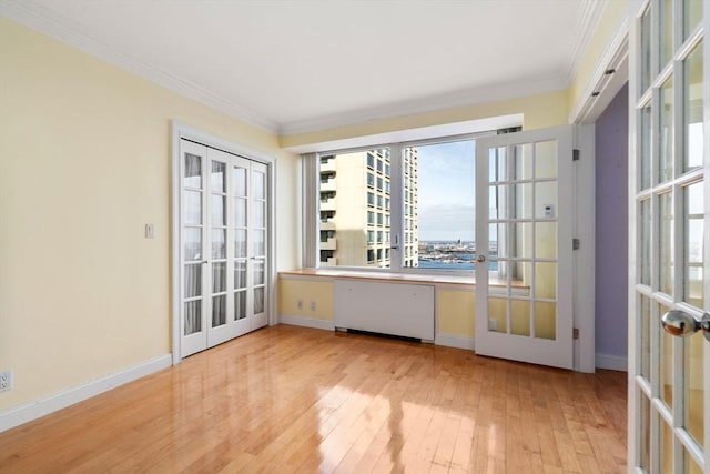 empty room featuring french doors, crown molding, and light wood-style floors