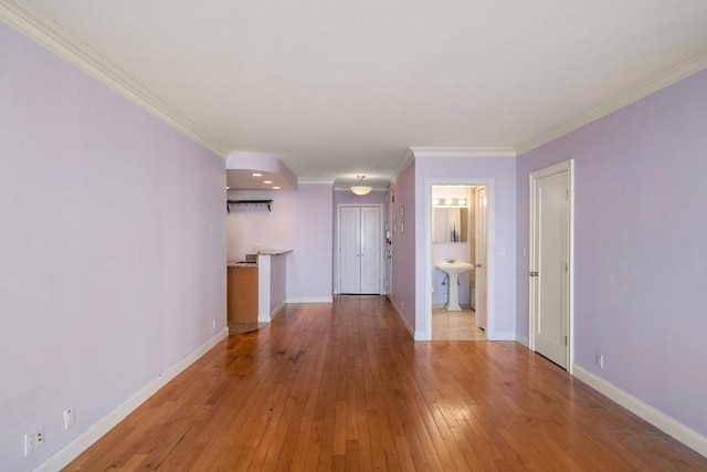 unfurnished living room featuring crown molding, baseboards, light wood finished floors, and a sink