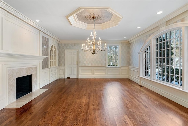 unfurnished dining area featuring a decorative wall, a premium fireplace, wood finished floors, ornamental molding, and an inviting chandelier