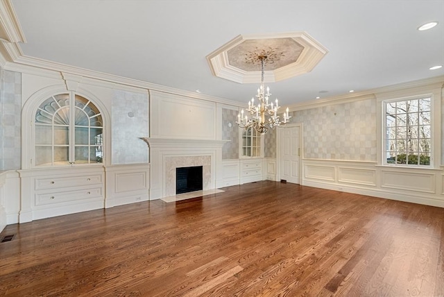 unfurnished living room with dark wood finished floors, a premium fireplace, crown molding, a decorative wall, and a notable chandelier