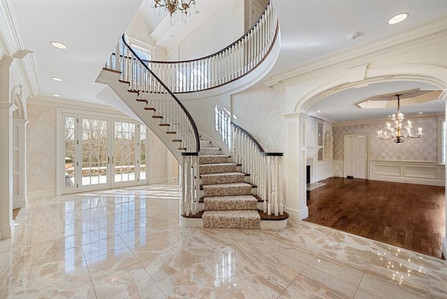 entryway with marble finish floor, stairs, crown molding, a decorative wall, and a notable chandelier