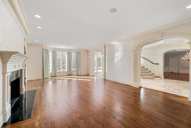 unfurnished living room featuring arched walkways, stairway, wood finished floors, and a high end fireplace