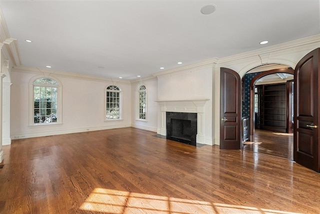 unfurnished living room with arched walkways, ornamental molding, a fireplace, and wood finished floors