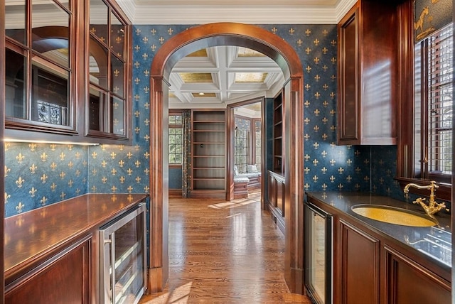 bar with wallpapered walls, beverage cooler, coffered ceiling, and a sink