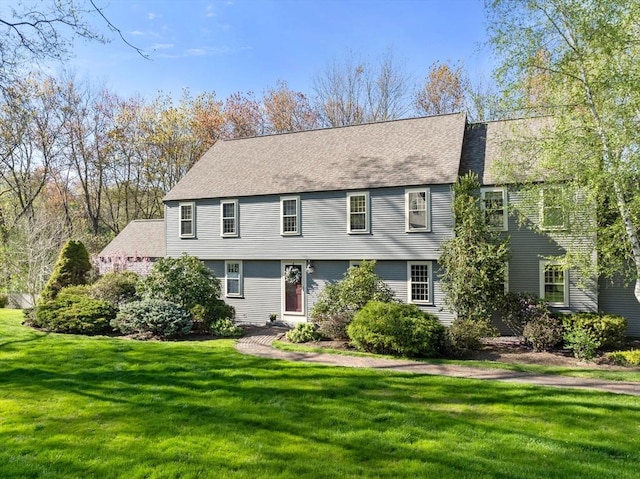 colonial-style house featuring a shingled roof and a front yard