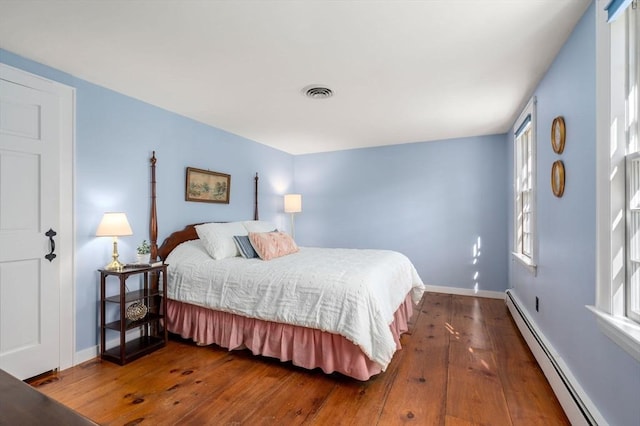 bedroom with a baseboard radiator, multiple windows, hardwood / wood-style flooring, and visible vents