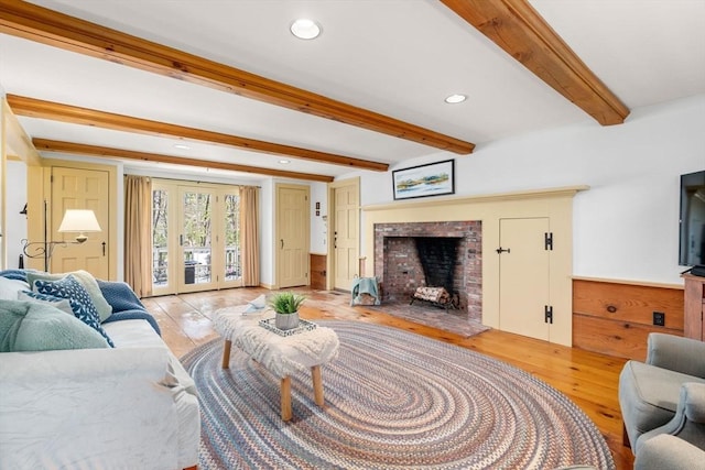 living area featuring beamed ceiling, light wood-type flooring, a fireplace with raised hearth, recessed lighting, and french doors