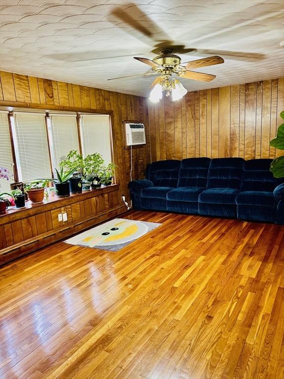 living area with a ceiling fan, an AC wall unit, wood walls, and wood finished floors