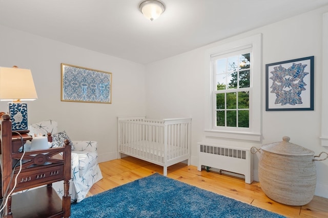 bedroom with a nursery area, radiator heating unit, and hardwood / wood-style flooring