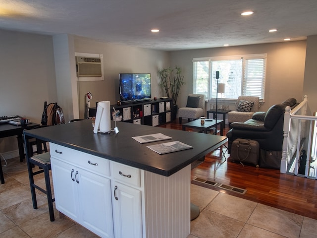 kitchen with a wall unit AC, white cabinets, a kitchen island, a kitchen breakfast bar, and light wood-type flooring