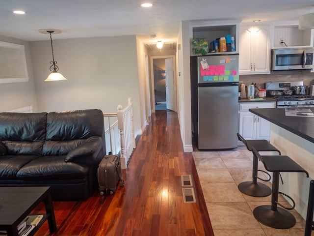 kitchen with appliances with stainless steel finishes, hanging light fixtures, white cabinetry, hardwood / wood-style flooring, and decorative backsplash