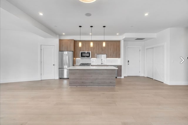 kitchen with pendant lighting, a kitchen island, light hardwood / wood-style floors, appliances with stainless steel finishes, and backsplash