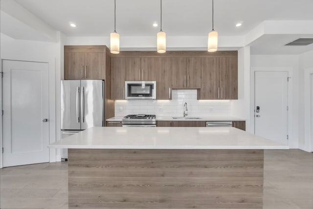 kitchen featuring stainless steel appliances, hanging light fixtures, sink, a center island, and backsplash