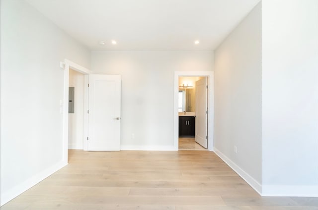 unfurnished bedroom with electric panel, connected bathroom, and light wood-type flooring