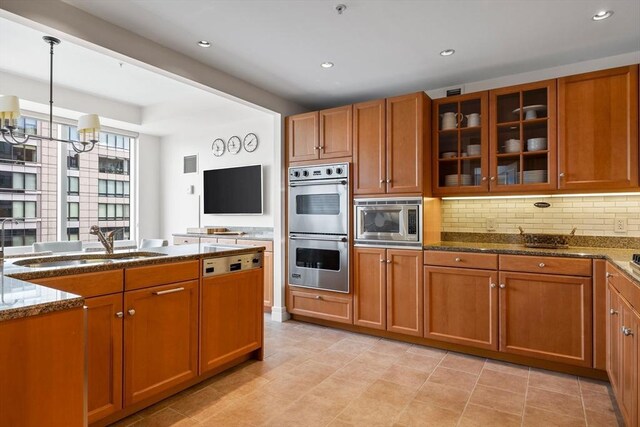 kitchen with stone counters, an inviting chandelier, sink, decorative backsplash, and appliances with stainless steel finishes