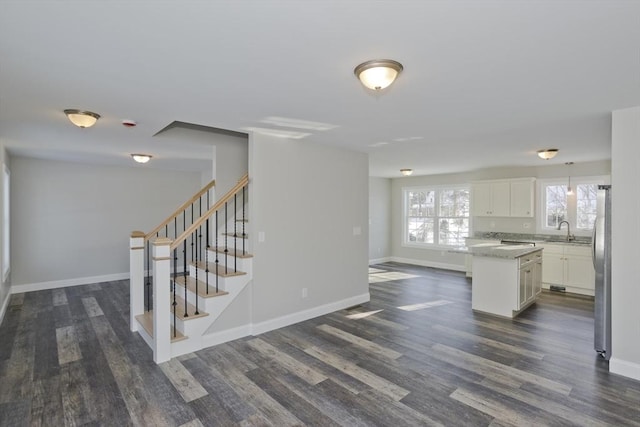 kitchen with sink, stainless steel refrigerator, white cabinetry, a kitchen island, and dark hardwood / wood-style flooring