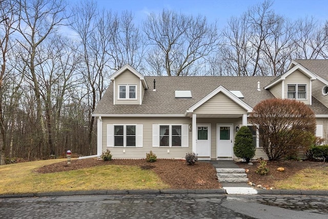 new england style home featuring a front yard and a shingled roof