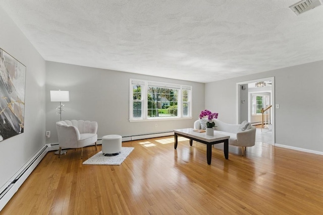 living room with a baseboard heating unit, wood finished floors, a textured ceiling, and baseboards