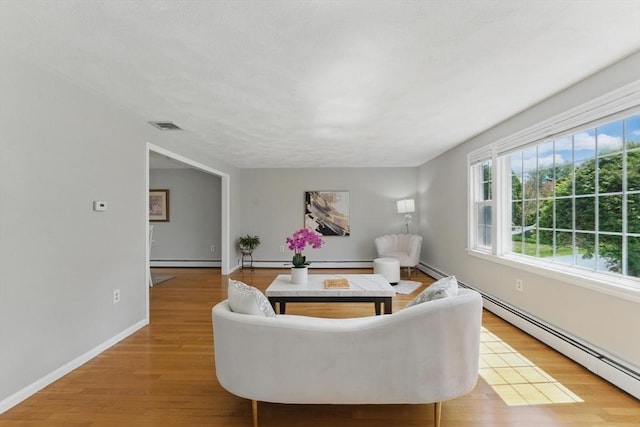 living area with light wood-style flooring, baseboard heating, a baseboard radiator, and baseboards