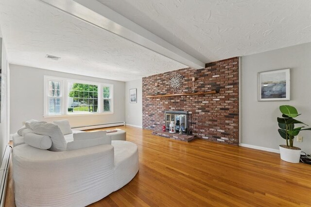 living area with wood finished floors, a textured ceiling, a baseboard heating unit, a brick fireplace, and baseboards