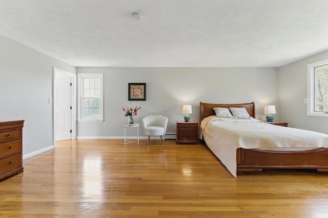bedroom with a baseboard radiator, light wood finished floors, and baseboards