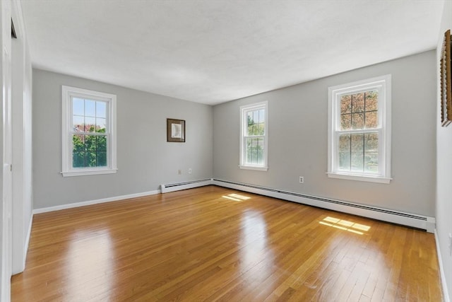 empty room featuring a baseboard heating unit, hardwood / wood-style flooring, and baseboards