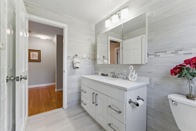 half bathroom with vanity, toilet, tile walls, baseboards, and wood finished floors