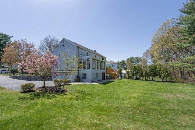 view of green lawn featuring driveway, a garage, and central air condition unit